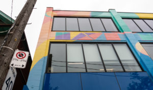 Close up photograph of the top corner of building where windows and a painted mural is seen. The mural features imagery of brightly coloured shapes, patterns and stylised font that reads "Have".