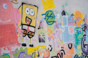 Close up photograph of a spray painted wall featuring a wide range of imagery from cartoon characters to geometric and organic patterns.