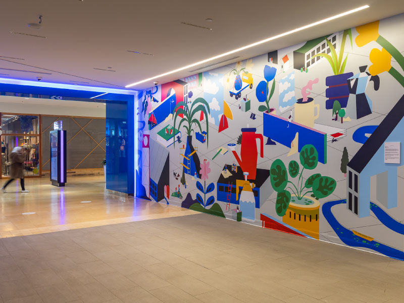 An interior mural inside of a mall by artist Adrian Forrow as part of the BMO National Mural Series by STEPS Public Art. Geometric and colour blocked illustrations of everyday items are depicted.