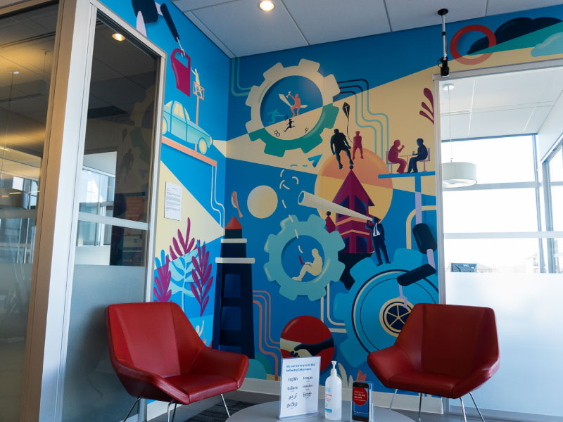 An interior digital vinyl mural by artist Zuna Amir in the corner of a bank with imagery of gears and people working to showcase busy work lifestyles. This is part of the BMO National Mural Series by STEPS Public Art