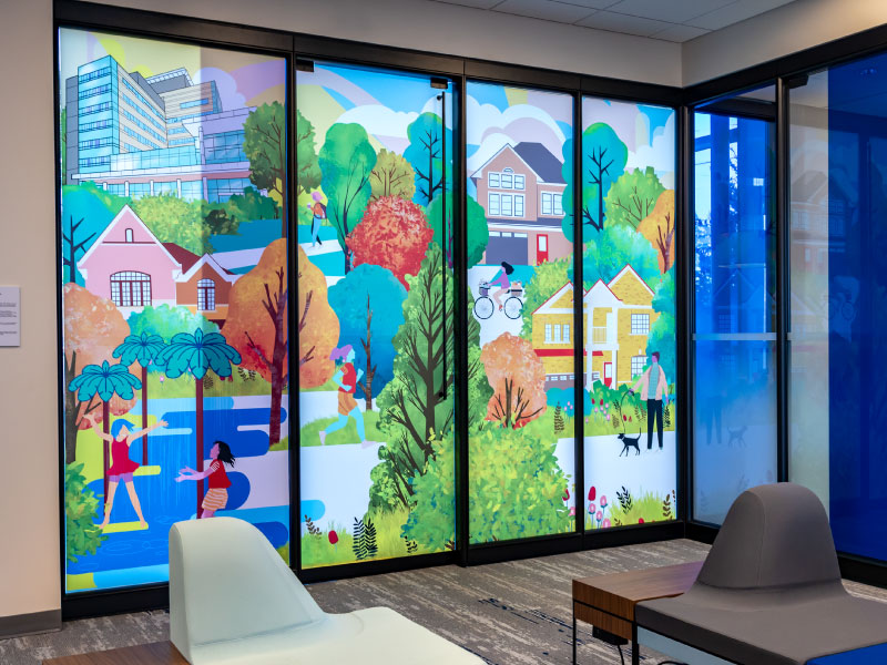 An interior translucent vinyl mural depicting a local neighbourhood with people playing in a waterpark and cycling by artist Asli Alin. This is part of the BMO National Mural Series by STEPS Public Art