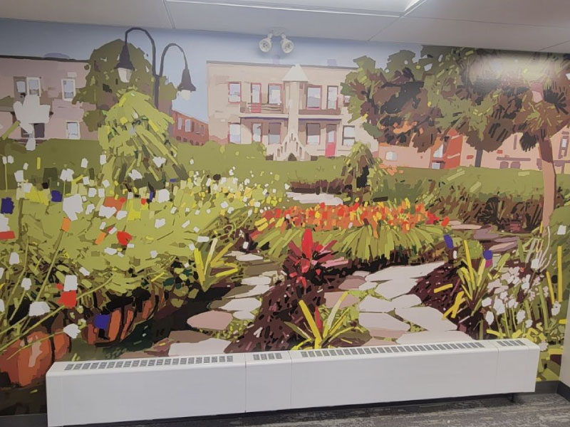 An interior digital vinyl mural by artist Bryan Beyung as part of the BMO National Mural Series by STEPS Public Art. The mural is in an impressionistic style of a garden behind a series of low rise apartments.