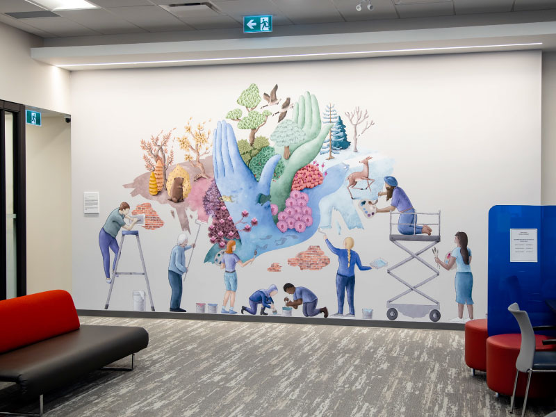 An interior digital vinyl mural by artist Keerat Kaur depicting a group of diverse people working together on a mural of a forest. This is part of the BMO National Mural Series by STEPS Public Art