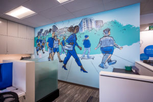 Photograph of an interior mural featuring imagery of figures walking on a path in an urban area painted in shades of blue and green installed in a BMO office.