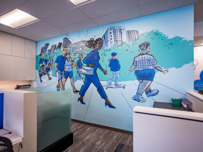 An interior digital vinyl mural by artist Matthew Salisbury of community members walking along a sidewalk wrapping around a city. This is part of the BMO National Mural Series by STEPS Public Art