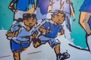 Close-up photograph of an interior mural featuring imagery of two children with bags running on a path.