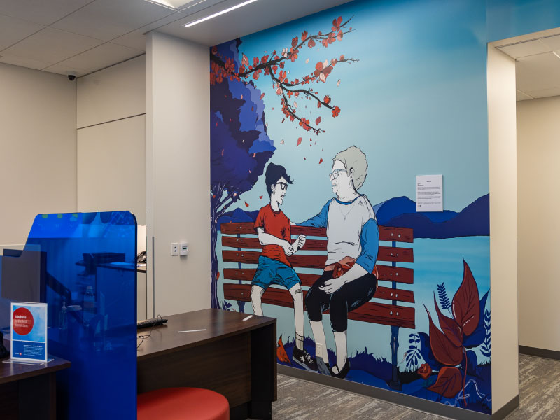 An interior vinyl mural by artist Ray Vidal of two people sitting on a bench in front of a lake and mountain view. This is part of the BMO National Mural Series by STEPS Public Art.