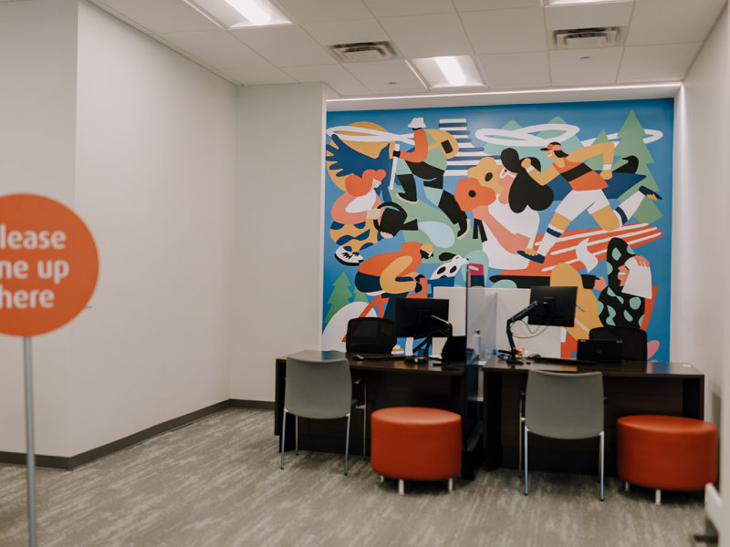 An interior mural depicting a collection of different people participating in activities in a bold and illustrative style by Rory Doyle as part of the BMO National Mural Series by STEPS Public Art