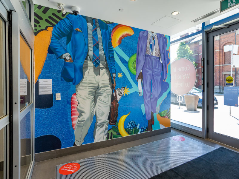 An interior vinyl mural at the entrance of a bank by artist Samara Shuter in a bold collage style of two people in suits going to work. This is part of the BMO National Mural Series by STEPS Public Art