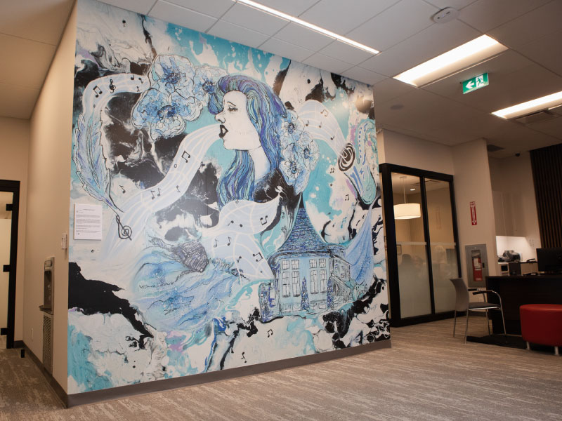 An interior digital vinyl mural by artist Wendy Reid in blue and black shades of whimsical illustrations of a woman singing and music notes swirling around as part of the BMO National Mural Series by STEPS Public Art