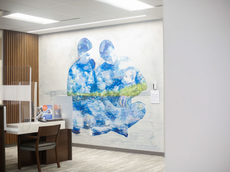 An interior digital vinyl mural by artist Alice Jennex as part of the BMO National Mural Series by STEPS Public Art. It depicts two people carrying a baby in blue watercolour style art.