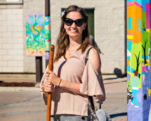 Artist Katherine Theresa Motigny smiling in Timmins, Ontario with her public art projects of painted street poles and boxes.