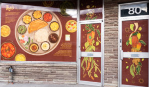 An empty storefront decorated with large public art window food art by Meegan Lim