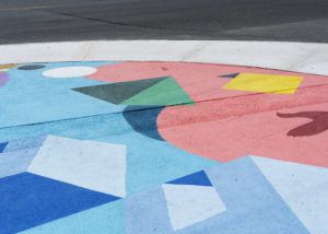 Close-up of a large ground mural by artist Andre Kan for Cooksville, Mississauga. The mural has geometric 3D shapes in blue, peach, green and yellow colours.