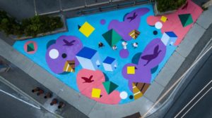 A shot from above shows artist Andre Kan and production team with ground mural