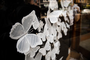 Close-up of a public art installation by Meghan Cheng with white butterflies in a storefront that light up in response to passersby