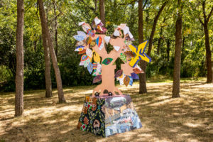 An outdoor sculpture of a tree on top of a base with collage images of Toronto, Rexdale, and the community. This was created by Quentin VerCetty and community members as part of From Weeds We Grow with STEPS Public Art