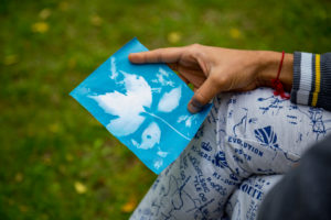 Close up of person holding a blue cyanotype print in a park.