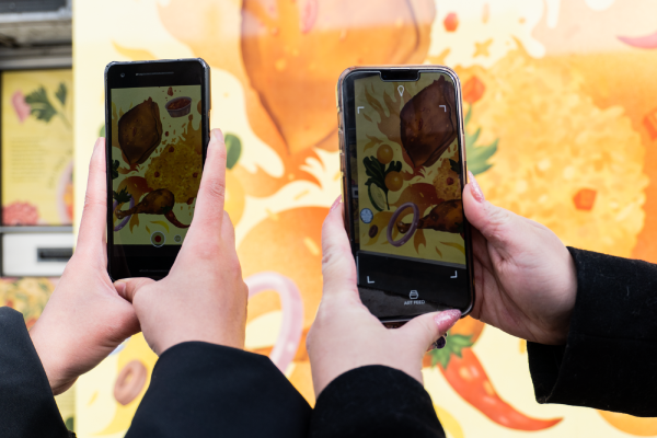Two people holding up mobile phones against a public art installation to enable AR components