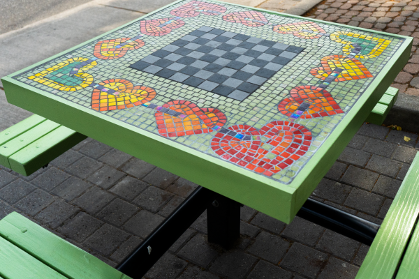 A square and green public picnic table adorned with mosaic artwork