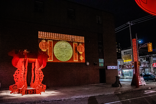 Large digital public art projection in Toronto's Chinatown against a brick wall in the evening. 