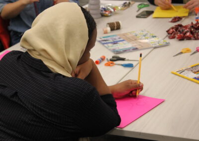 A participant at a table drawing on pink paper, with supplies on the table.