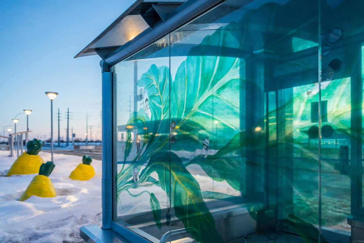 A public transit stop and station with public artwork showcasing human figures at work on sugar beet leaves