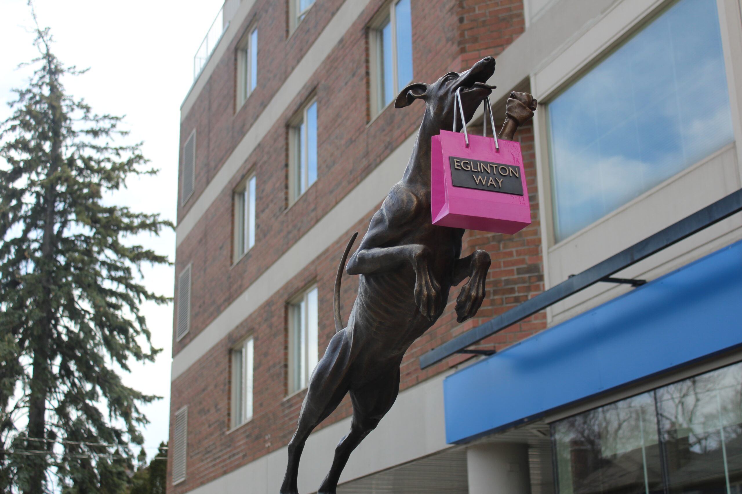 A sculpture by William Hung of a dog leaping forward with a shopping bag in its mouth that says Eglinton Way BIA