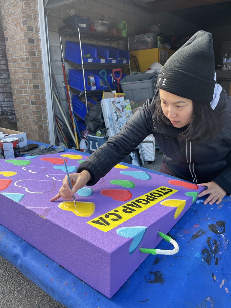 Artist Amanda Lederle is painting a purple StopGap accessible ramp with hearts as part of STEPS Public Art's Accessible Art and Placemaking project