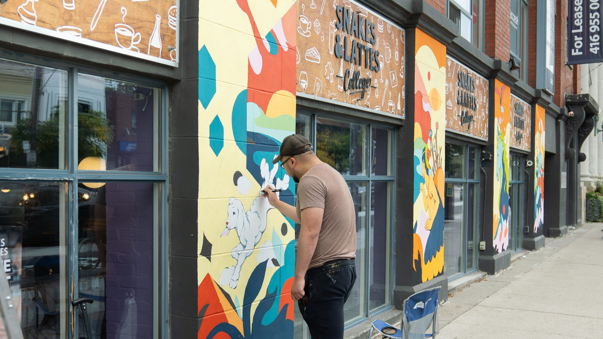 Artist Jinke Wang painting a mural on the exterior of Snakes and Lattes College in Toronto