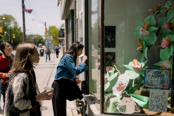 Three people gazing into a storefront with public art in the windows by artists Hour Studio Space and STEPS Public Art