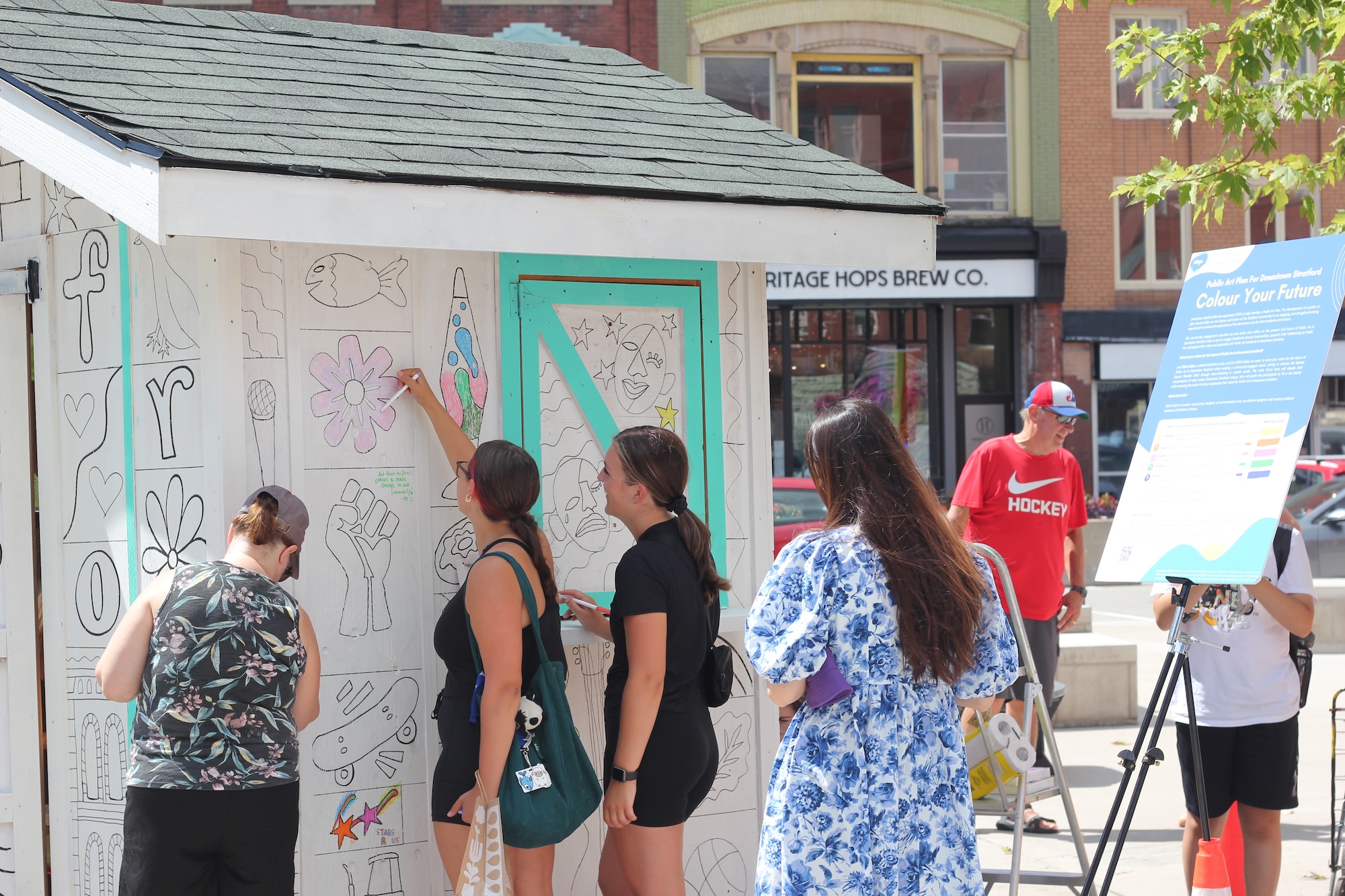 Community members drawing art on a wooden shed in Downtown Stratford as part of a public art community consultation by STEPS Public Art