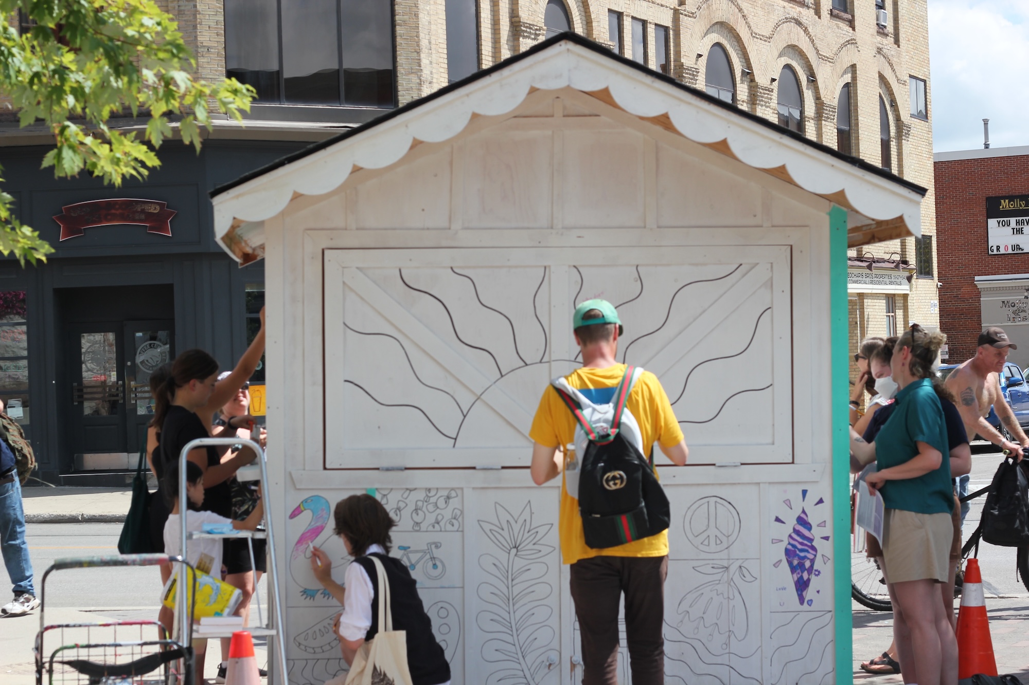 Families putting artwork on a wooden shed in Downtown Stratford as part of a community engagement by STEPS Public Art