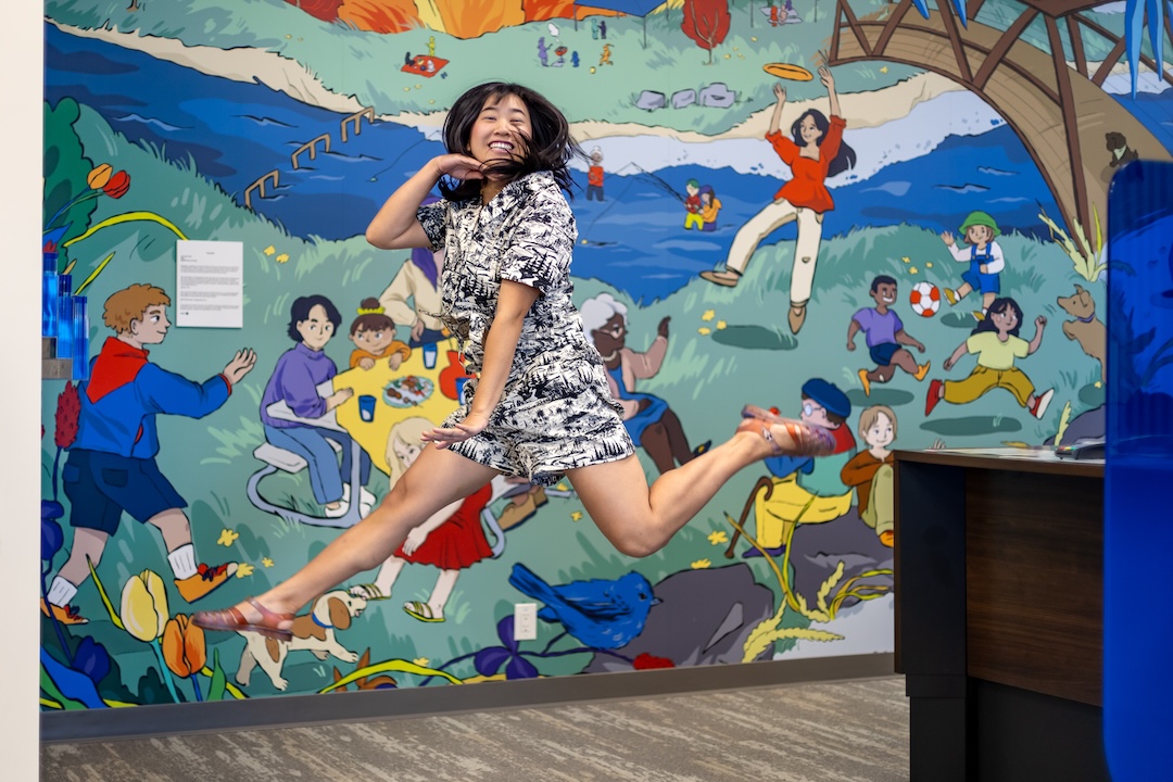 Artist Yen Linh Thai happily jumping in front of her interior mural as part of the BMO National Mural Series by STEPS Public Art
