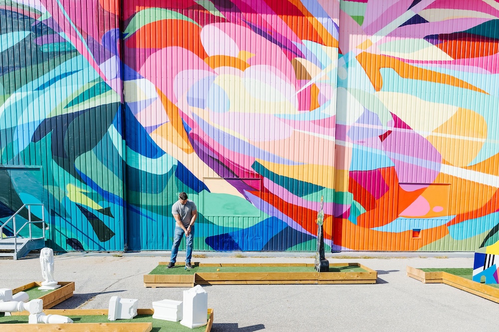 A public art mini golf course with a colourful mural in the background as part of community installations by STEPS Public Art and Northcrest Developments