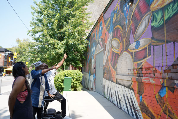 Three people gazing at a mural that includes an audio component as part of a project by STEPS Public Art and the Bloor Annex BIA in Toronto