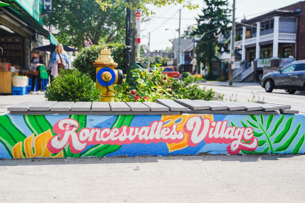 A painted public bench with artwork that says Roncesvalles Village as part of a project with STEPS Public Art