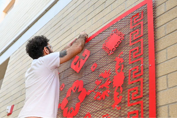 Roda Medhat hanging sculptural artwork onto a brick wall as part of the STEPS Public Art residency