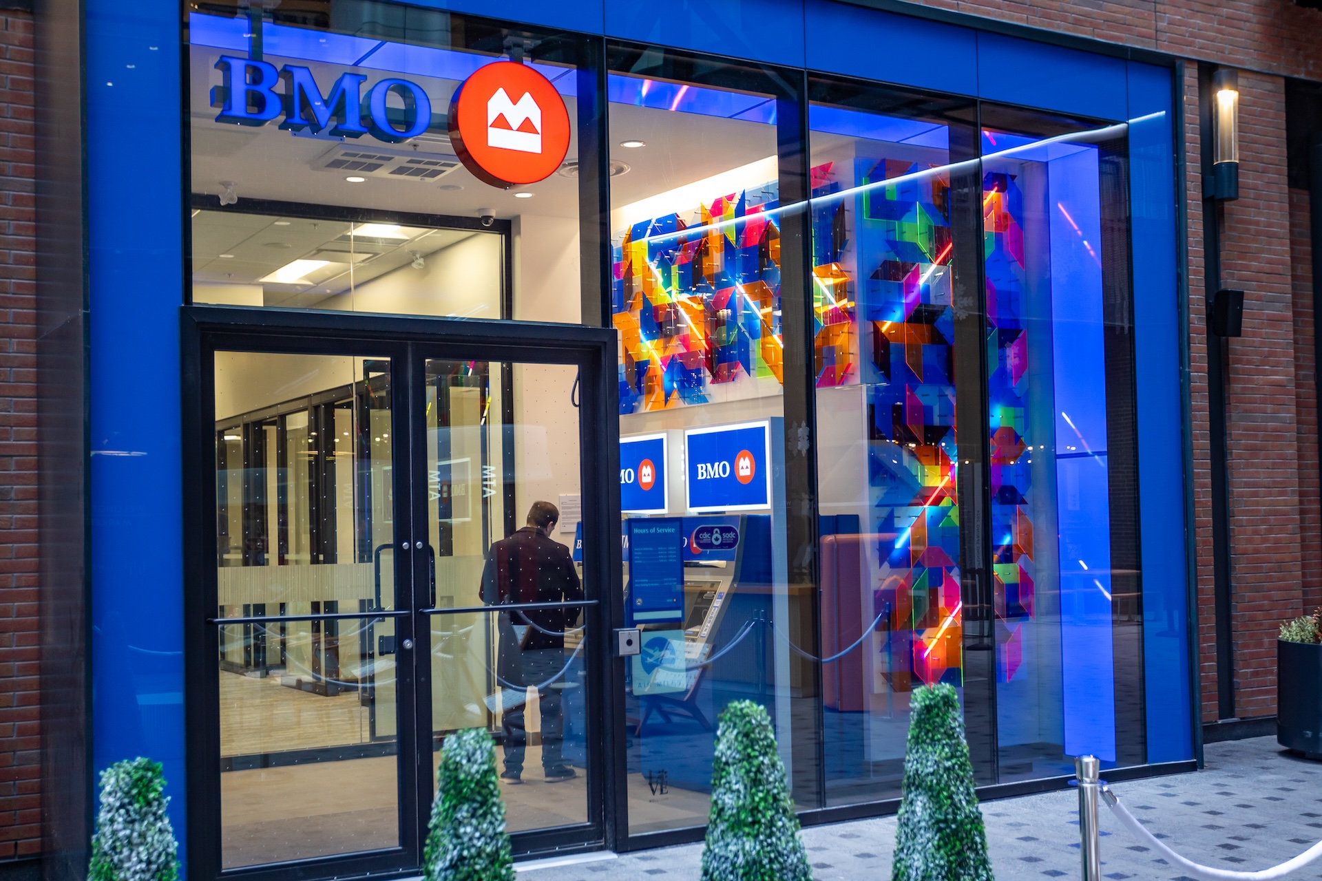 A BMO bank with large glass windows that peer into the ATM lobby. A geometric 3D plexi and light installation is installed as part of the BMO National Mural Series by STEPS Public Art